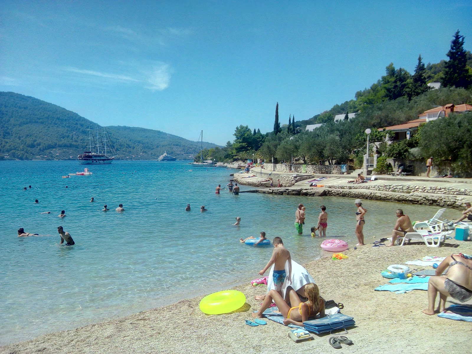 Shallow turquoise water at Plitvine pebble beach near Vela Luka, Korčula, with families swimming